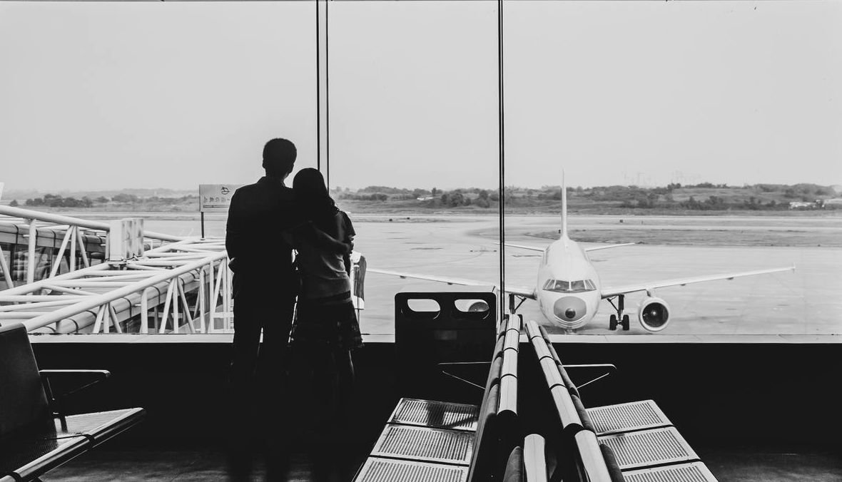 Travellers waiting at an airport terminal with an aircraft visible outside